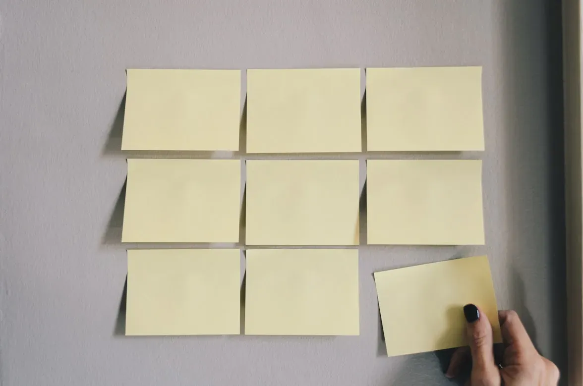 Mural com post-its amarelos organizados em uma grade 3×3, sendo que uma mão está posicionando um post-it no canto inferior direito.