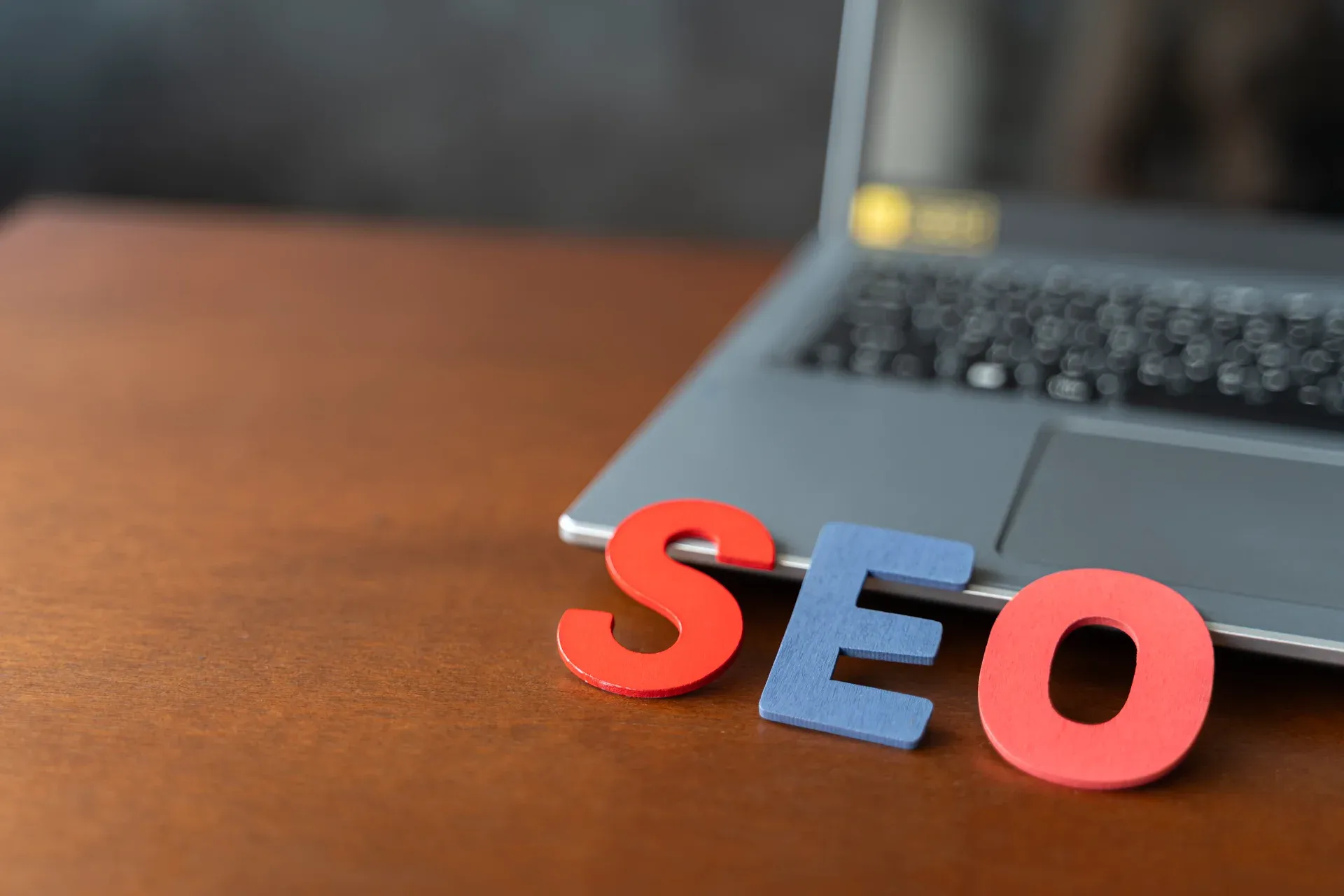 Letras de madeira formando a palavra SEO apoiadas em um notebook