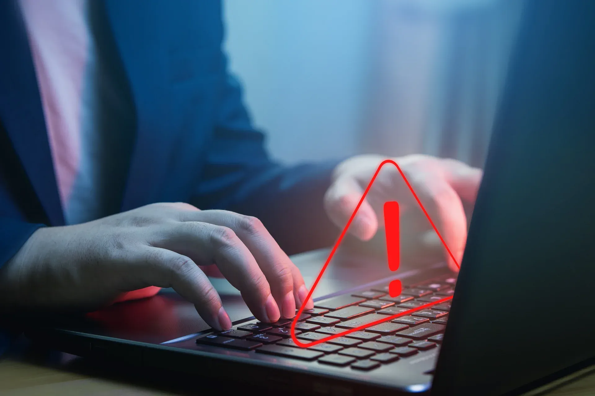 Mãos digitando em notebook com ícone de alerta vermelho sobre o teclado