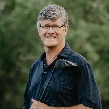 Photo of Barry Gibson holding golf club in front of out of focus trees