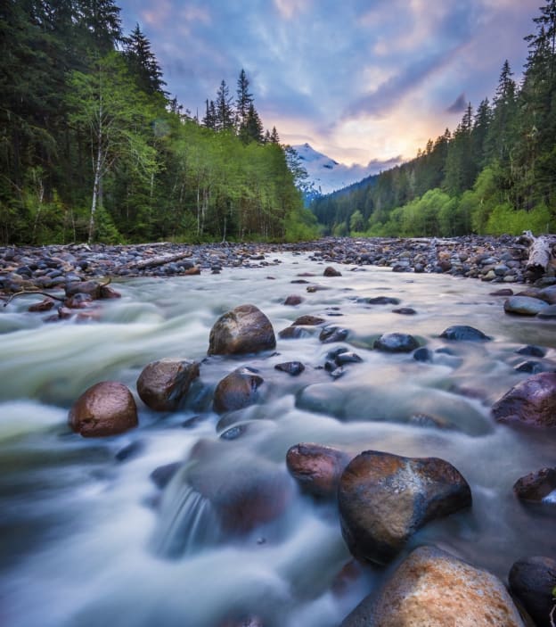 Image 9-21-25 at 5.39 PM River flowing at dusk, through rocks with mountains in the background and trees alongside the river.