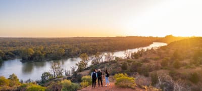 Three travellers gaze at the winding Murray River at sunset, beginning a road trip to the Mallee outback.