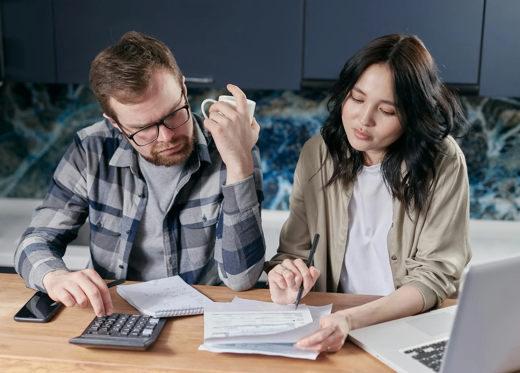 Couple at kitchen table reviewing paperwork and using a calculator — weighing the costs and ROI of a whole-home generator installation