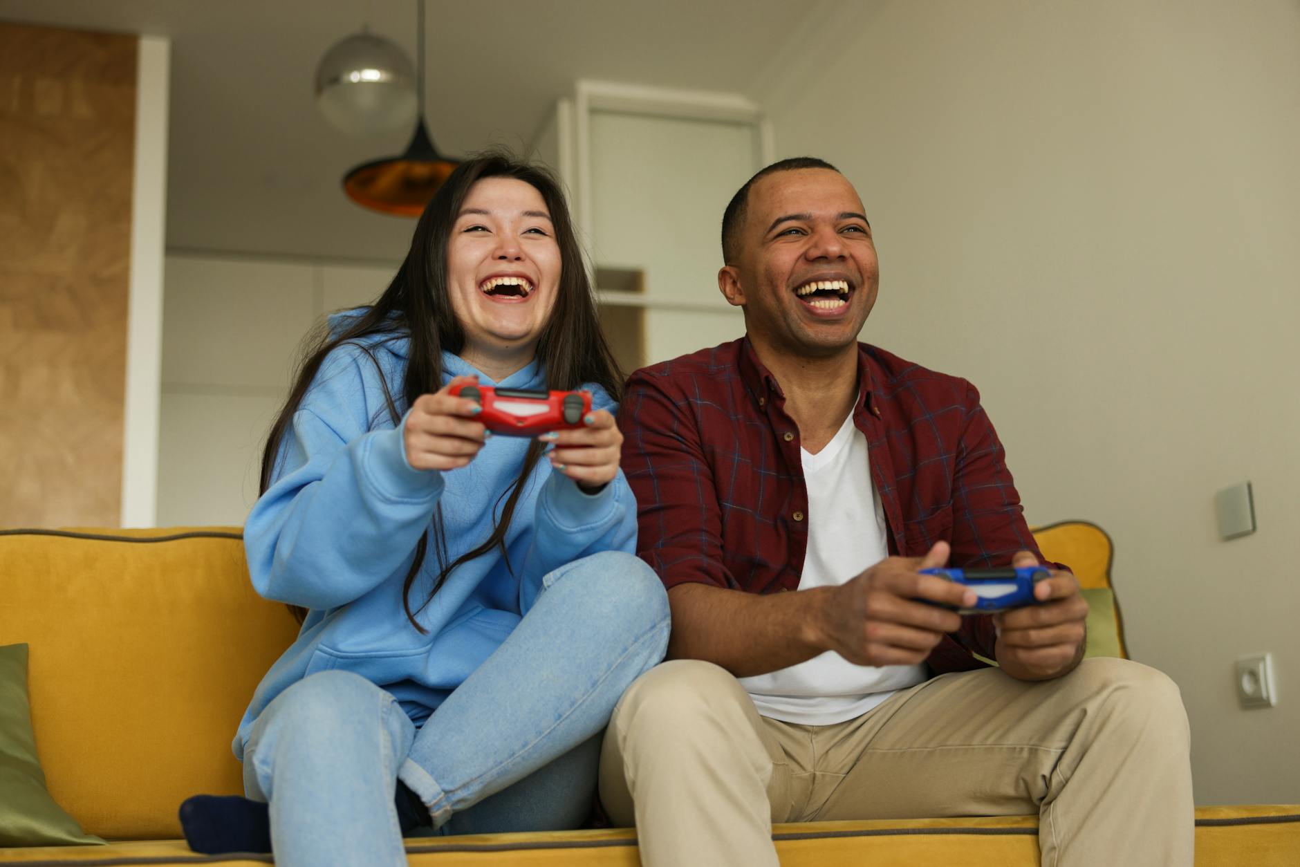 Two people laughing together on a couch with game controllers
