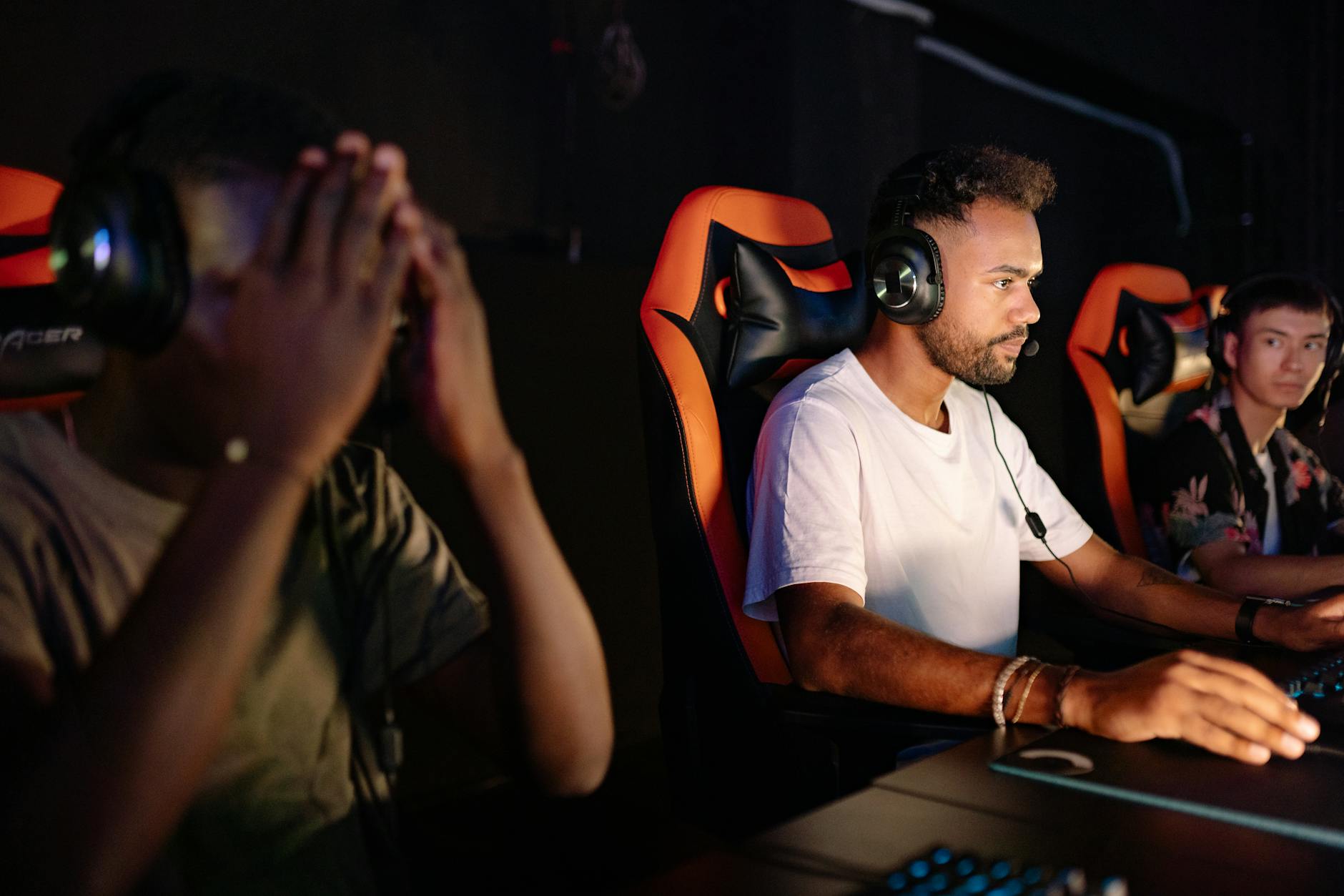 Three young men gaming together at a LAN event with headsets and gaming chairs