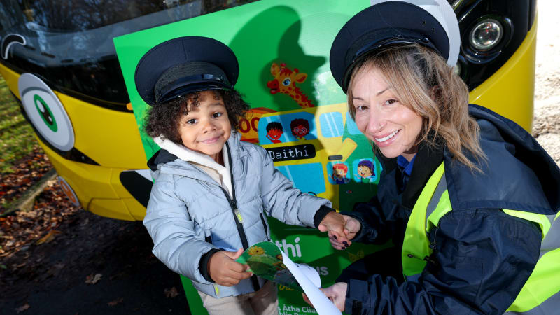 Child and Dublin Bus employee in driver caps pose with papers in front of colorful children's themed Dublin Bus