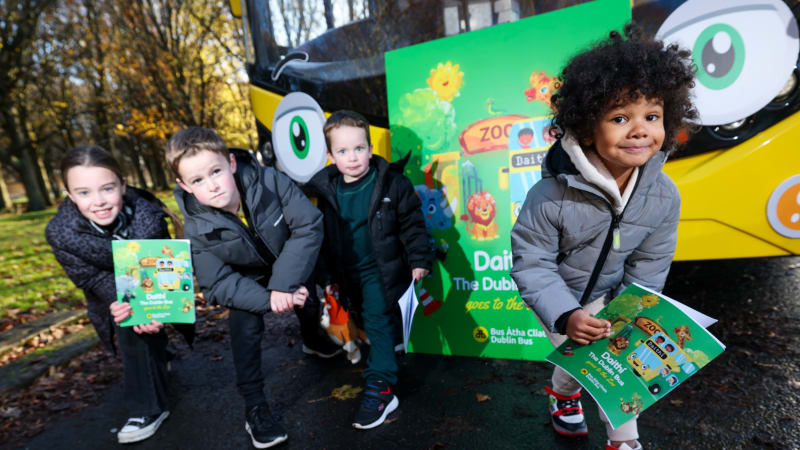 Four children holding Daithí The Dublin Bus children's books standing next to a decorated yellow Dublin Bus at zoo event