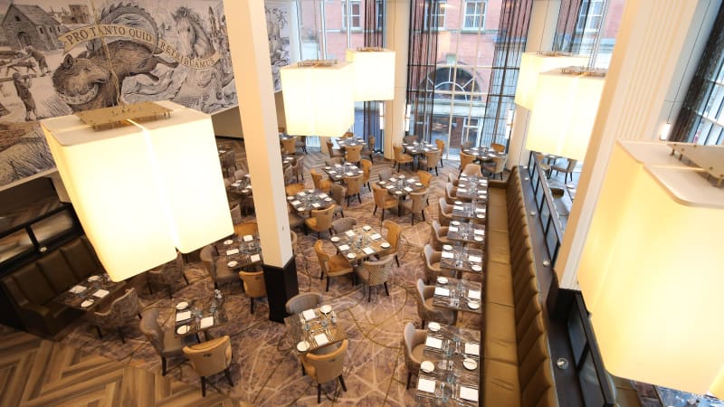 Upscale restaurant dining room with high ceilings, pendant lights, and wildlife mural