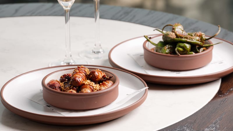 Two terracotta bowls with glazed pearl onions and blistered peppers topped with sesame seeds