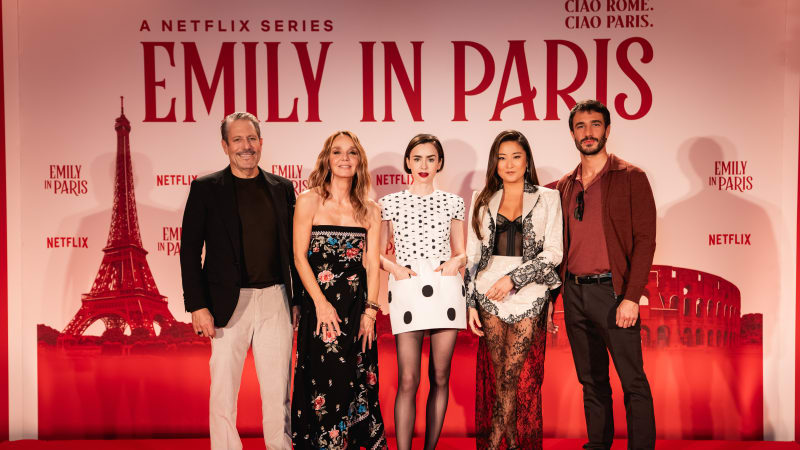Five cast members posing at the Emily in Paris Netflix press conference with red backdrop