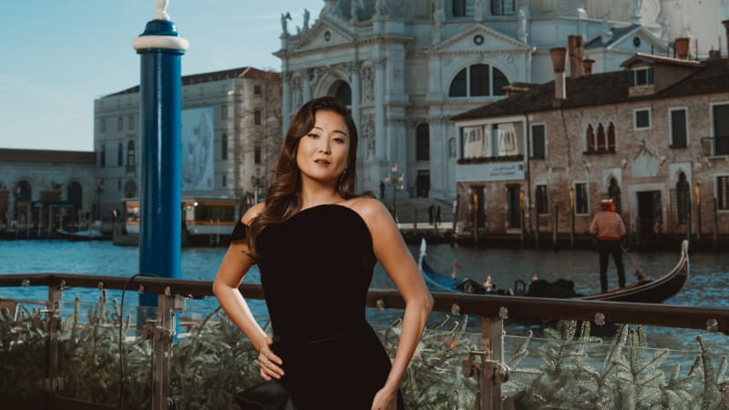 Woman in black one-shoulder dress posing by Venice canal with Santa Maria della Salute church in background