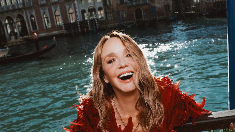 Woman laughing in red feathered outfit by Venice's Grand Canal with gondola in background