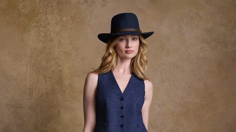 Woman in navy blue tweed waistcoat and matching wide-brimmed hat against neutral background
