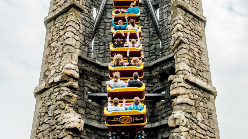 Roller coaster with riders ascending between medieval stone towers at Emerald Park theme park