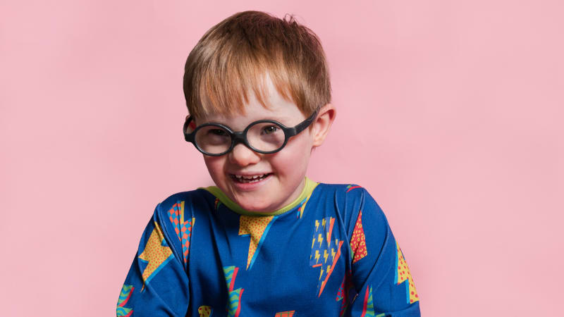 Ted, a young boy with glasses wearing a colorful blue lightning bolt patterned top, smiling