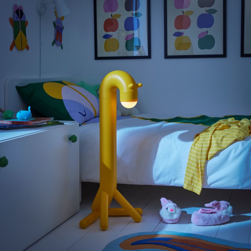 Yellow giraffe-shaped children's floor lamp illuminating a cozy kid's bedroom at night with colorful decor