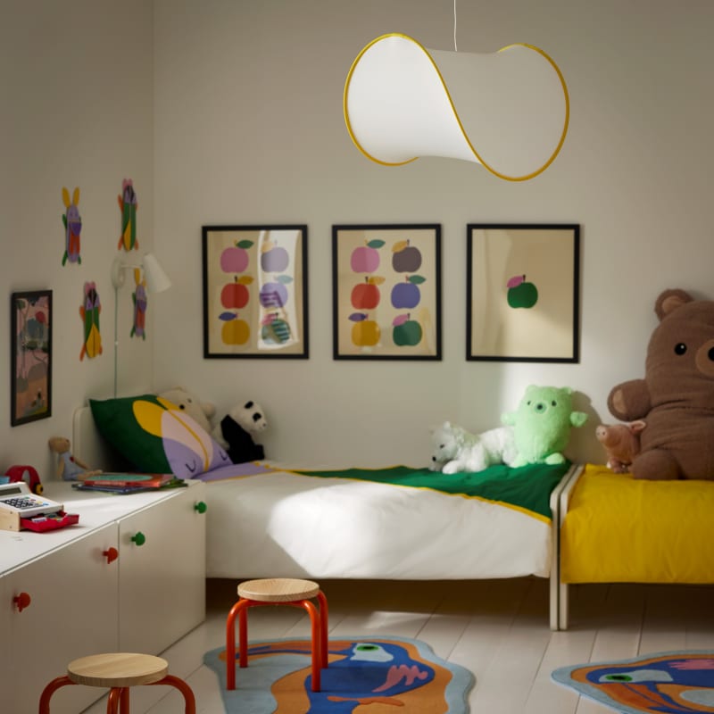 Colorful children's bedroom with yellow bed, stuffed animals, apple artwork, and wavy pendant light
