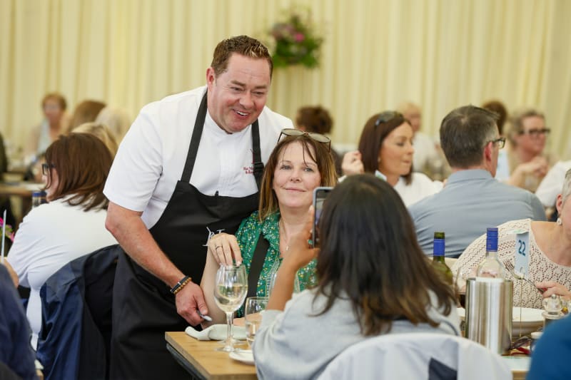 Chef in white jacket and black apron chatting with guests at elegant dining event