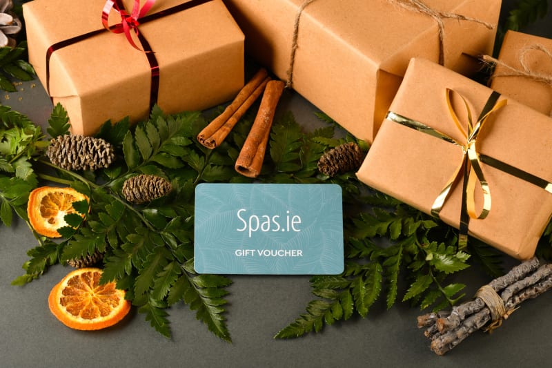 Spas.ie gift voucher card surrounded by kraft paper wrapped presents, ferns, cinnamon sticks and dried oranges