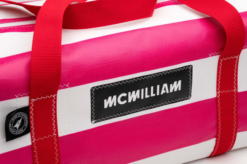 McWilliam pink and white striped duffle bag with red handles and black branded label