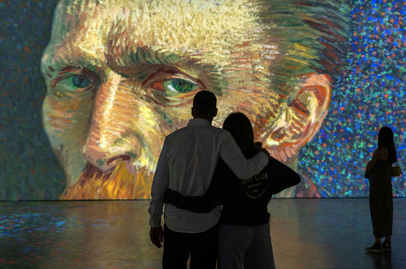 Couple embracing while viewing large Van Gogh self-portrait projection at immersive art exhibition