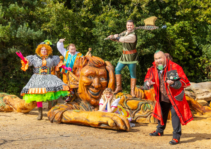 Jack and the Beanstalk pantomime cast in costume posing with giant wooden sculpture outdoors
