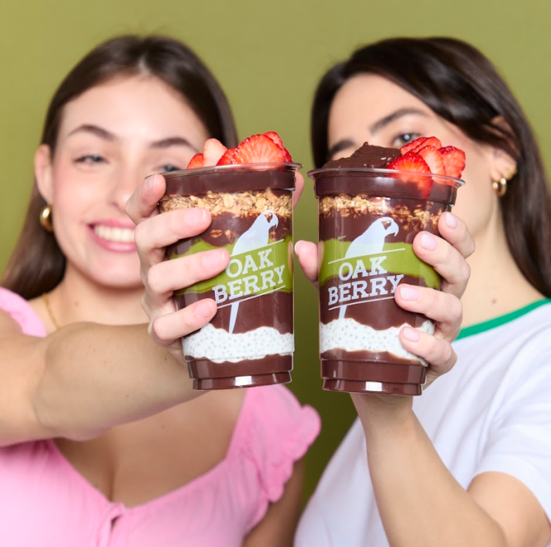 Two women holding Oakberry açaí cups with layered chia pudding, granola and strawberries