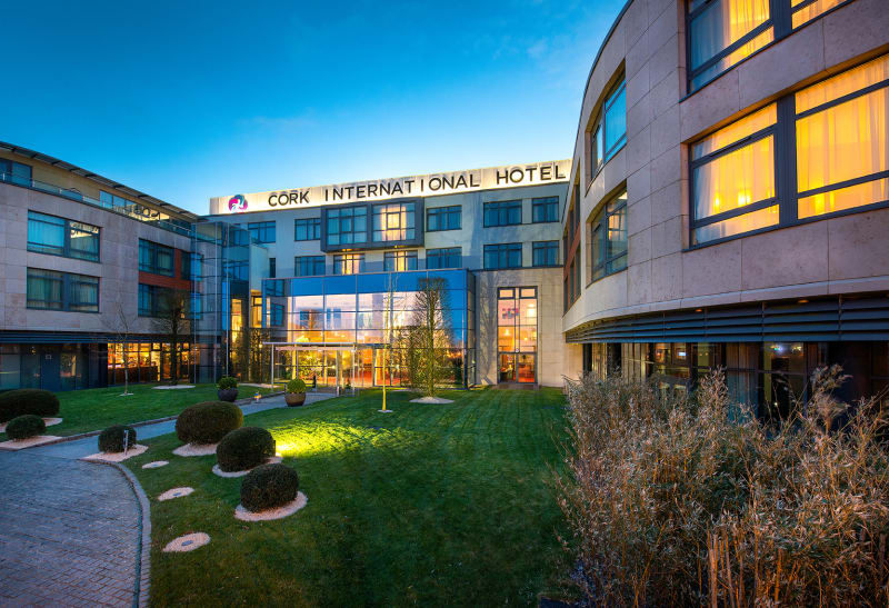 Cork International Hotel exterior at dusk with modern curved architecture and landscaped courtyard garden