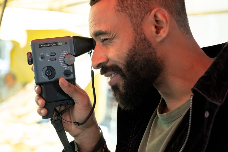 Man with beard smiling while looking through Fujifilm Instax Mini Evo camera viewfinder