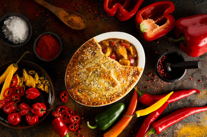 Chicken curry pot pie with sesame crust surrounded by colorful peppers and spices on dark surface