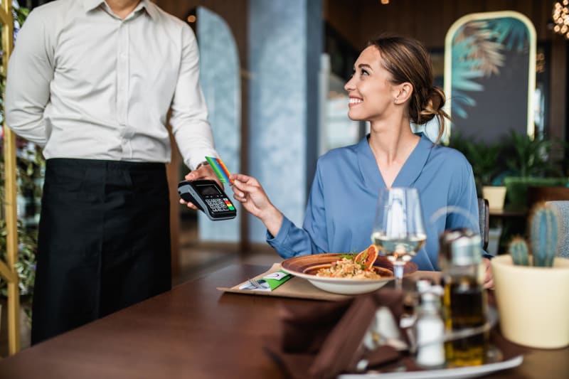 Woman paying for restaurant meal with contactless card payment to server holding terminal