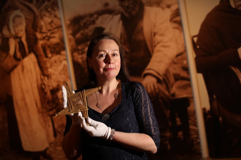Clodagh Doyle holding a traditional woven straw St. Brigid's Cross in front of historical photograph