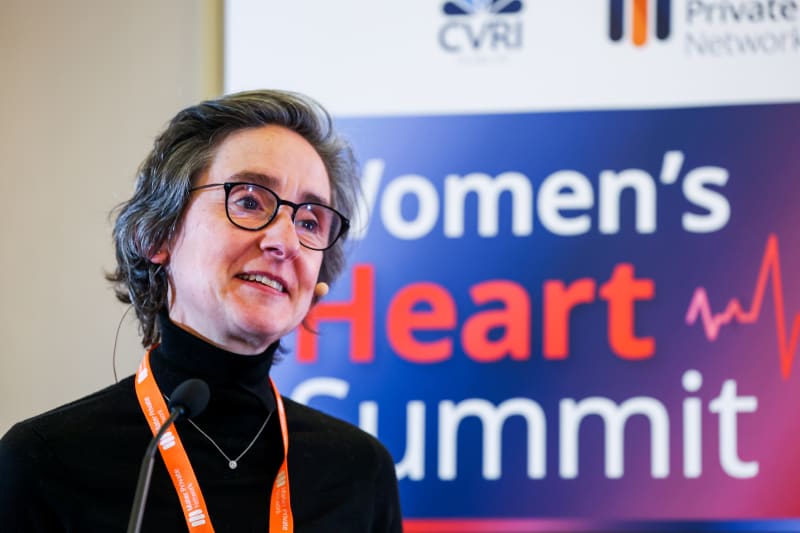 Speaker at Women's Heart Summit presenting at podium wearing black turtleneck and orange lanyard