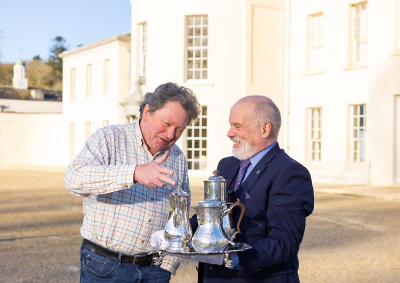 Two men examining antique silver tea service on a tray outside Mount Congreve historic building