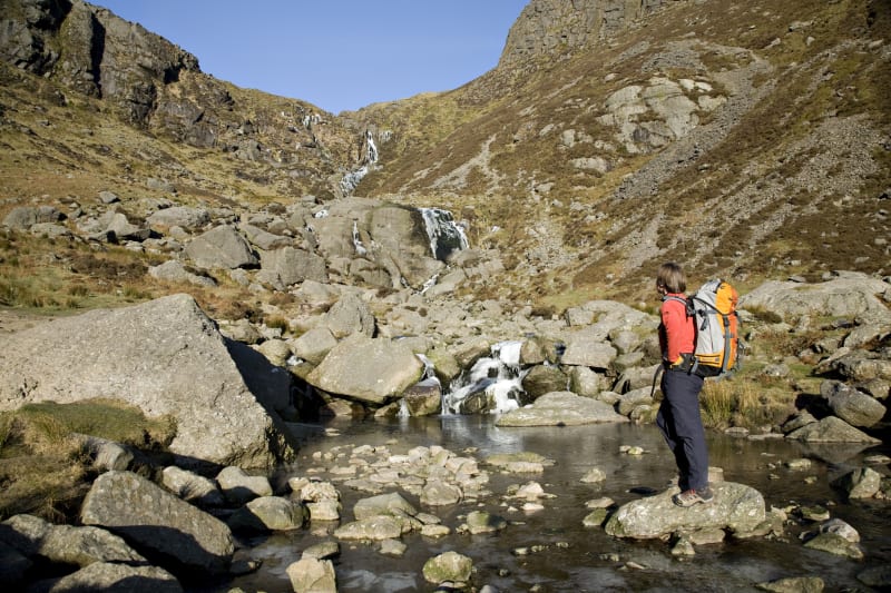 Hiker in orange jacket viewing Mahon Falls waterfall in Comeragh Mountains, Co Waterford