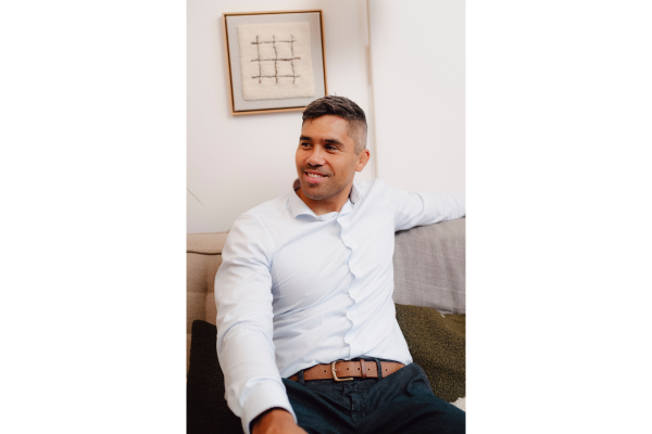 Man in light blue shirt sitting relaxed on a sofa, smiling and looking to the side