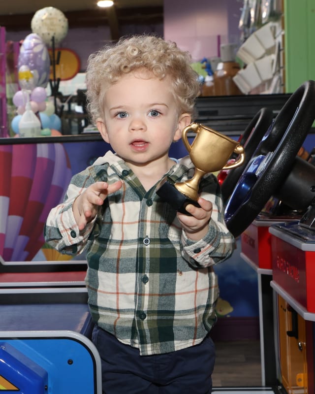 Tiernan McGrane holds a golden trophy at an arcade or entertainment venue