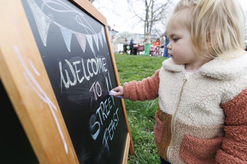 Young child writing on a chalkboard welcome sign for Street Feast outdoor event