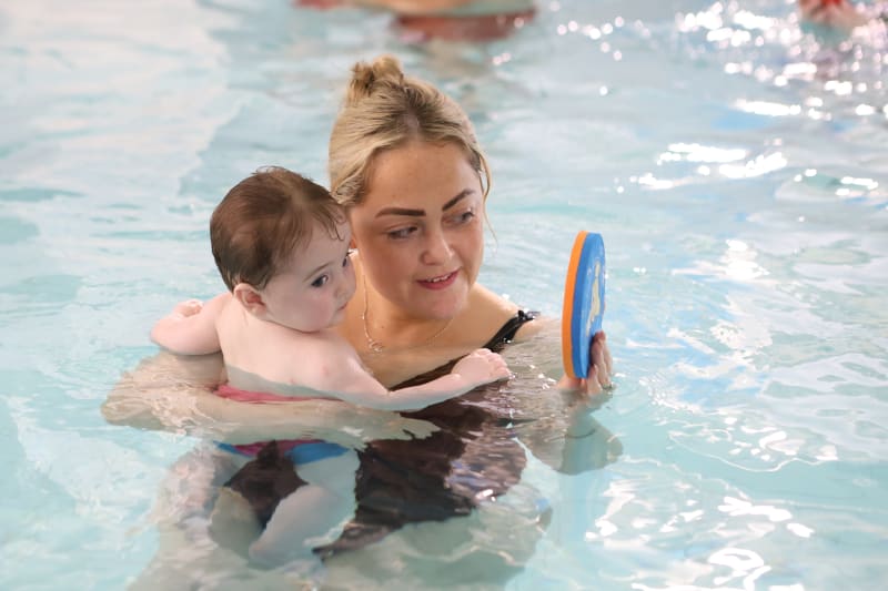 Woman and child in swimming pool with flotation device during swim lesson