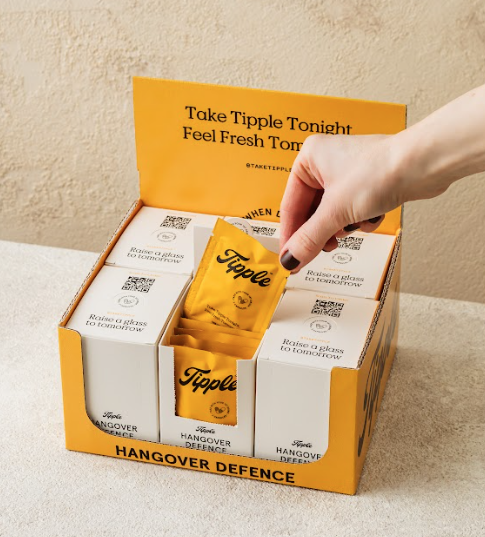 Hand selecting packet from Tipple hangover defence product box with white and orange sachets