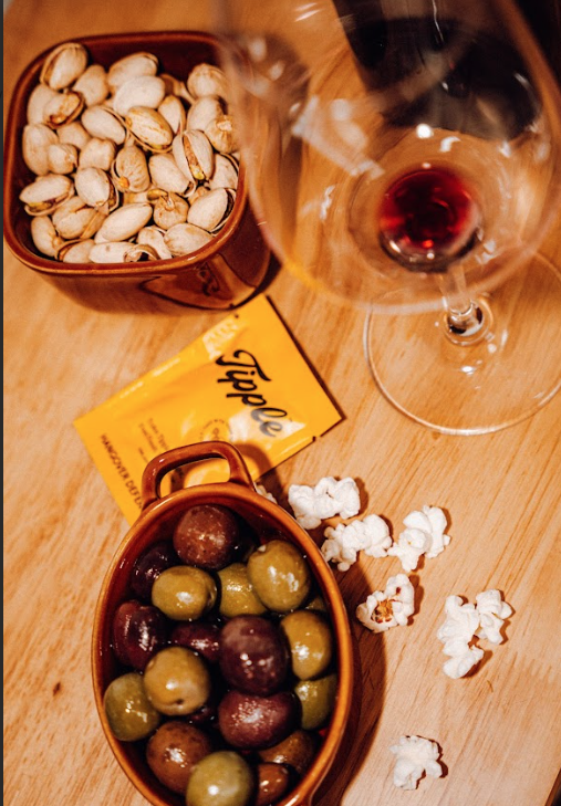Appetizer spread with nuts, olives, wine glass and Tipple branded snack package on wooden surface