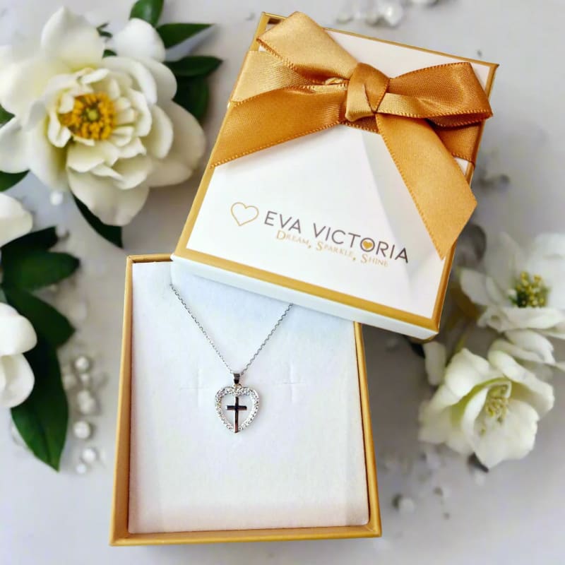 Heart-shaped cross pendant necklace in Eva Victoria jewelry gift box with gold ribbon and white flowers