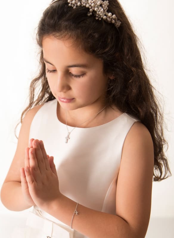 Eva A in white dress with pearl headband, hands in prayer position wearing cross jewelry