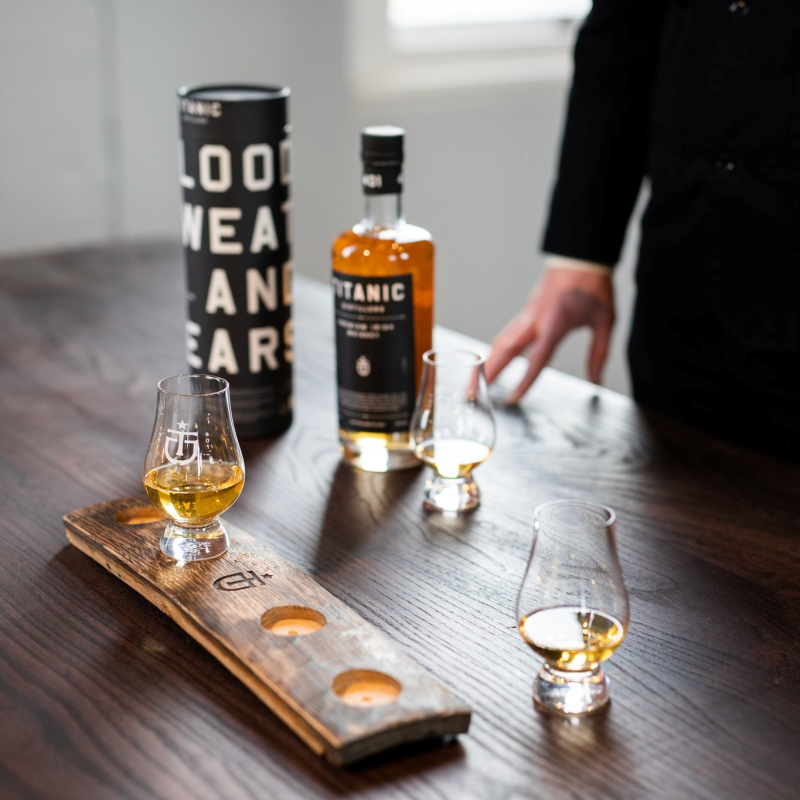 Titanic Distillers Irish whiskey bottle and tasting flight with three Glencairn glasses on a wooden bar.