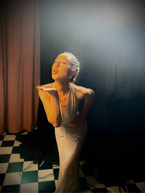 Woman in silver halter gown blowing a kiss on a checkered floor with dramatic backlighting.