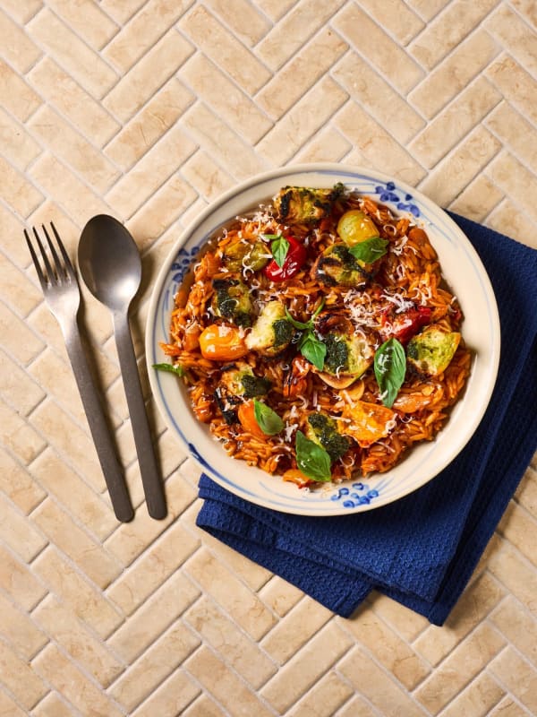 Bowl of tomato and chorizo orzo with roasted broccoli, cherry tomatoes, basil and grated cheese.