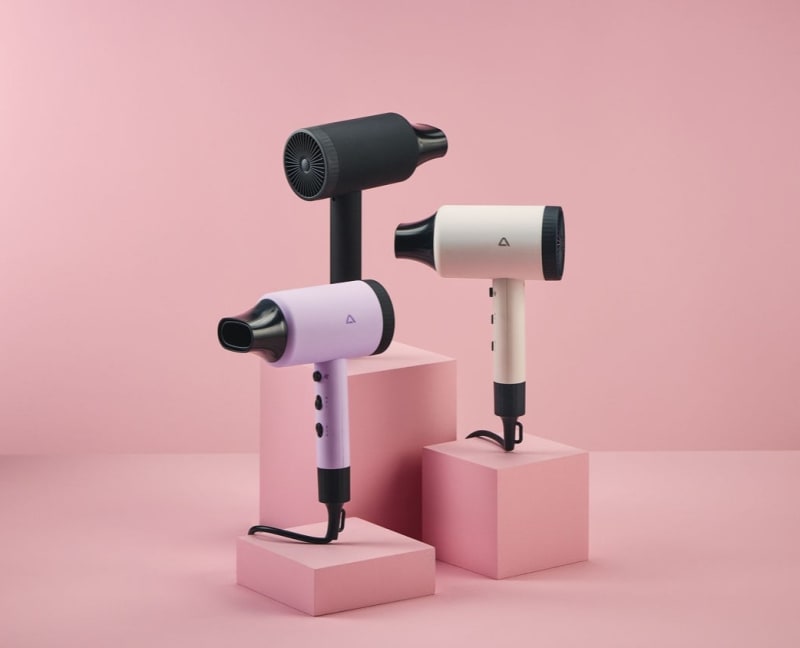 Three Ambiano Ionic Hairdryers in black, lavender and white displayed on pink plinths against a pink background.