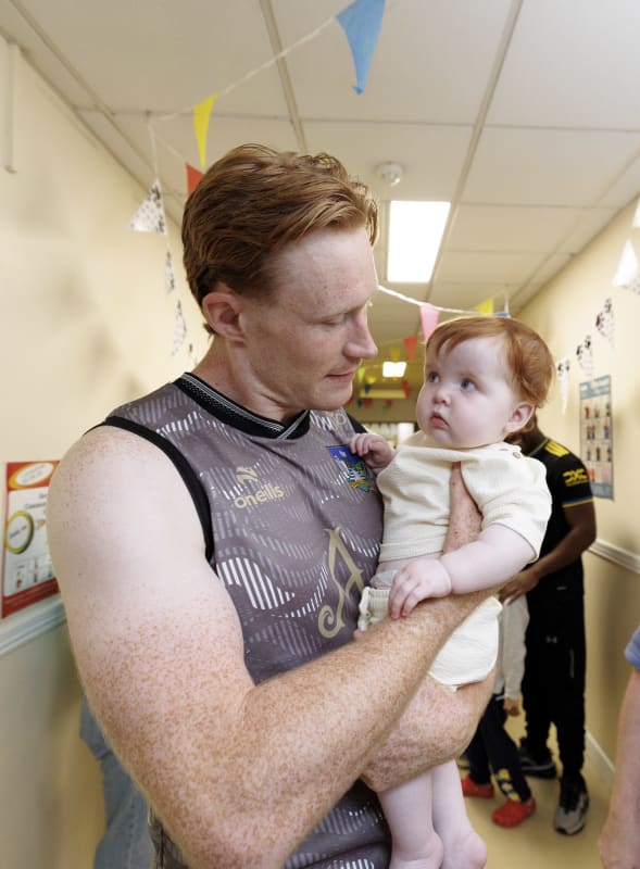 Limerick GAA player holding a red-haired baby in a decorated hospital corridor during a visit to Crumlin Hospital.