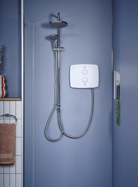 White electric shower unit mounted on blue-grey bathroom wall with chrome rail, rainfall head and handheld shower hose.