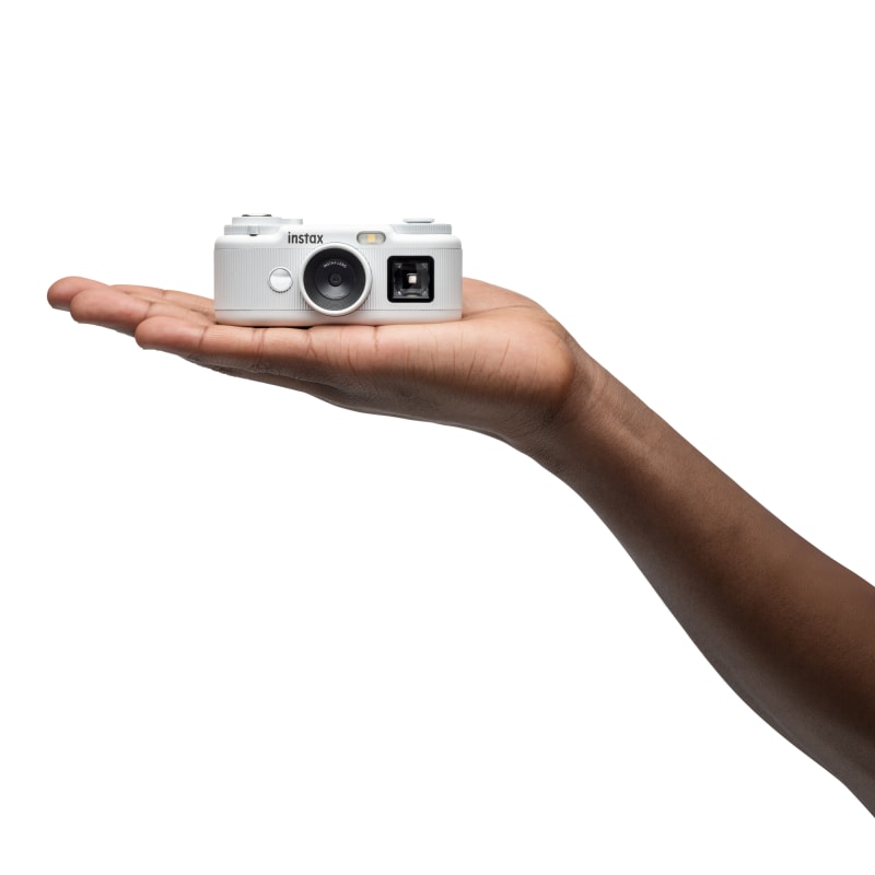 Fujifilm instax Pal 2 White mini compact camera resting in the palm of a hand, shown against white background.